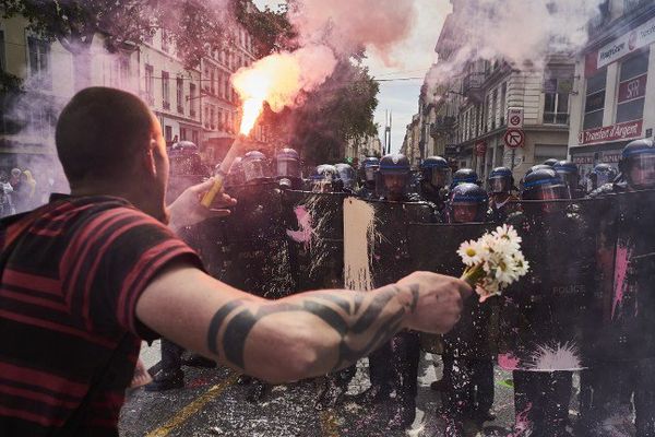 Un manifestant portant à la fois un fumigène et des fleurs fait face aux forces de l'ordre lors de la manifestation lyonnaise du 26 mai 2016.   