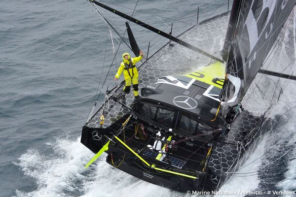 Alex Thomson (GBR) sur son Imoca Hugo Boss au large des Iles Kerguelen, survolé par la frégate Nivose de la Marine Nationale Française