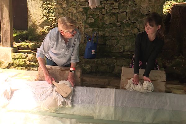 Une bénévole initie une jeune fille à laver un drap dans un lavoir.