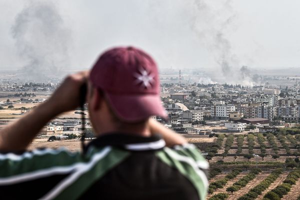 Depuis la ville turque de Sanliurfa, un homme regarde aux jumelles les panaches de fumées au-dessus de la ville syrienne de  Ras al-Ain, de l'autre côté de la frontière.