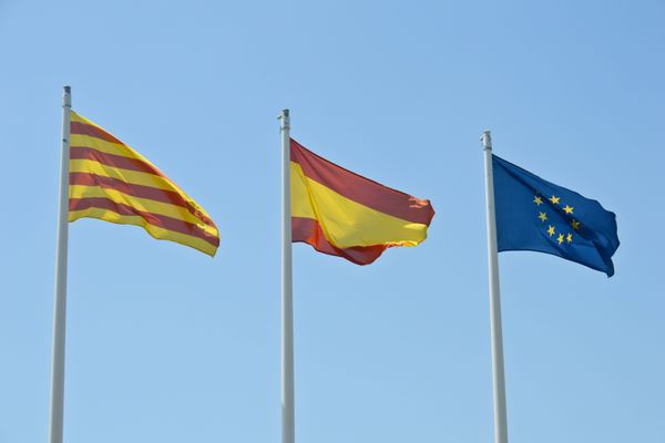 A gauche, le drapeau officiel de la région de Catalogne flottant aux côtés des drapeaux espagnol et européen.