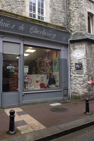 Devant l'emblématique boutique de parapluies du 1" rue du port à Cherbourg, Claire Yvon partage des anecdotes du tournage des "Parapluies de Cherbourg" à Pauline Conte,  présentatrice de l'émission de France 3 Normandie.