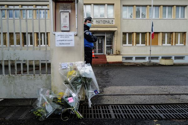 Un gendarme monte la garde près de bouquets de fleurs déposés devant l'entrée de la gendarmerie d'Ambert (Puy-de-Dôme) le 23 décembre 2020. 