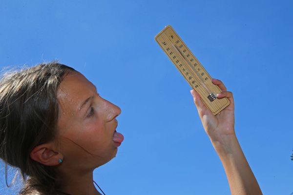 Une jeune fille transpire et regarde le thermomètre qui affiche des températures record.