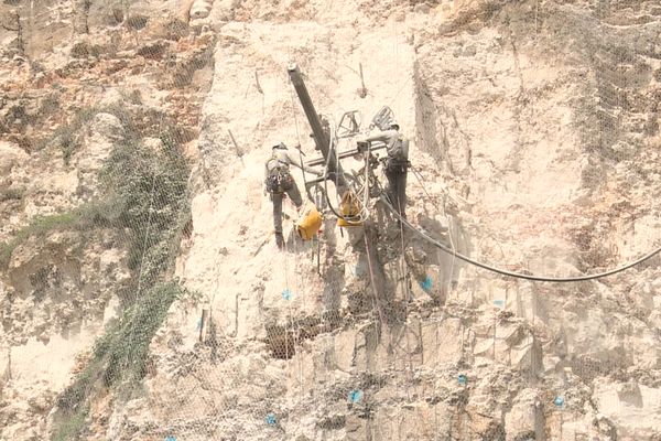 Les cordistes confortent la falaise en forant la roche