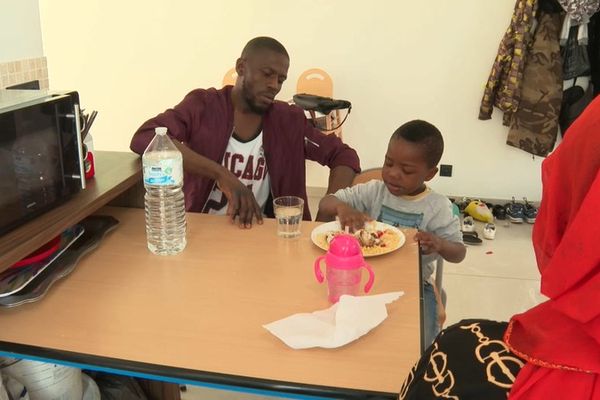 Entouré de sa mère et de son père, Abdoulaye déguste son repas à la maison