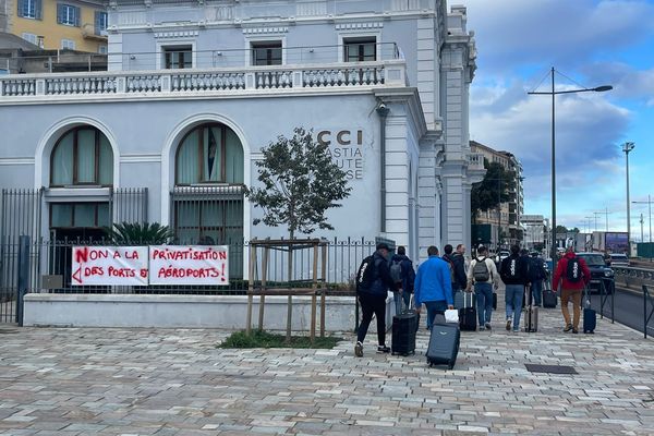 Des passagers quittent le port de Bastia, bloqué, et passent devant le siège de la Chambre de commerce de Haute-Corse.