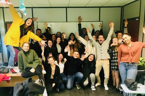 L'enseignante est sur la table à gauche de la photo, avec un gilet jaune