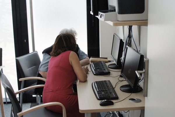 Une assistante et une personne agee devant un ecran d'ordinateur dans une salle.