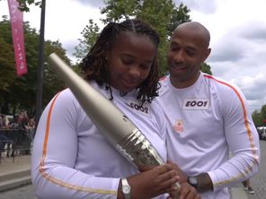 Thierry Henry, ancien capitaine de l'équipe de France de football, passe la main à Romane Dicko pour le relais de la flamme olympique sur les Champs-Élysées, ce dimanche 14 juillet.