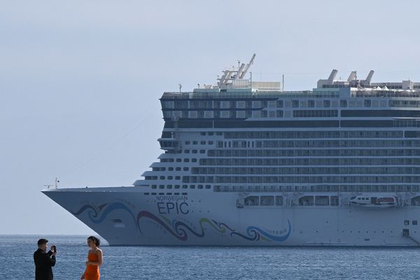 Cannes (Alpes-Maritimes) : une jeune femme pose devant un bateau de croisière de la compagnie norvégienne Epic qui navigue dans la baie de Cannes.