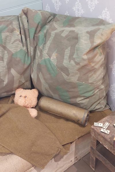 Sommier de lit, confectionné avec la toile de jute de sacs à provisions de l'armée anglaise, duvets fabriqués à partir de couvertures réglementaires de l'armée américaine, bouillotte constituée d'un extincteur et d'une douille d'obus de l'armée américaine, lampe de chevet comprenant une grenade MK2 de l'armée américaine