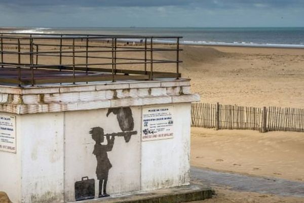 Photo prise le 29 décembre 2015, une oeuvre d'art protégée par du plexiglas réalisée par le street-artist Banksy représente un enfant transportant une valise et un télescope, avec un vautour perché dessus. Un hommage aux migrants et réfugiés sur la plage de Calais.