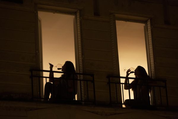 Une jeune femme boit à son balcon, pendant le confinement - Photo d'illustration 