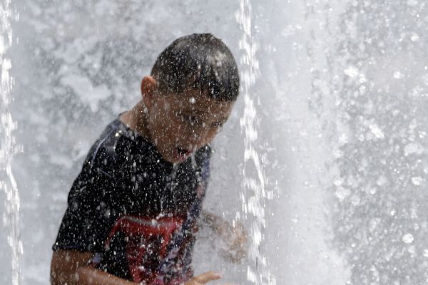 Un enfant se rafraîchit dans une fontaine. 