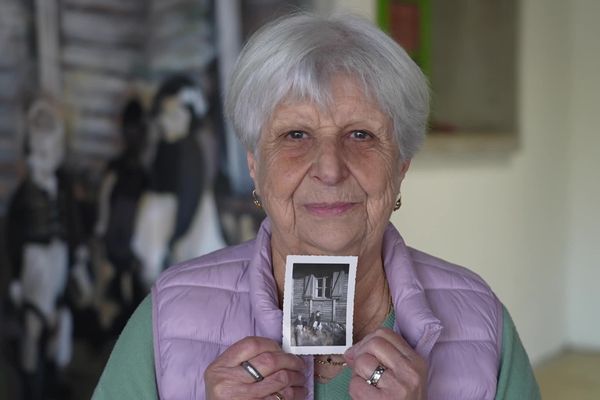 Annette Rénaud, épouse Rigon, aujourd'hui âgée de 78 ans, pose devant la fresque de l'école primaire d'Oradour-sur-Glane qui la représente aux côtés de son petit-frère. Entre ses mains, la photo originelle prise au début des années 1950.