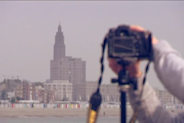 Un photographe sur la plage du Havre avec, en fond, l'église Saint-Joseph