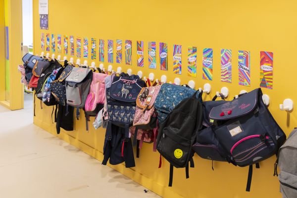 Des cartables alignés dans un couloir d'école primaire.