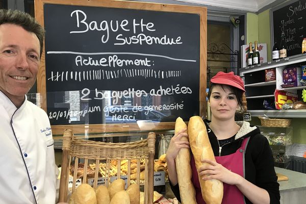 Christophe Ponseel et son employée, Anaïs Geneviève, devant l'ardoise indiquant la règle et le nombre de baguettes suspendues.