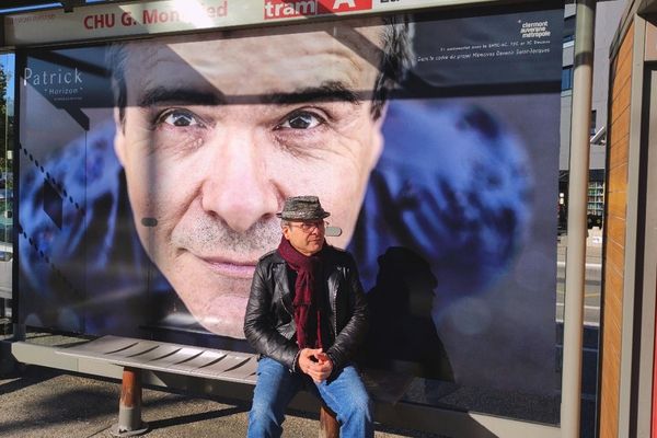 Patrick Foulhoux, habitant depuis ses 11 ans dans le quartier Saint-Jacques, assis devant son portrait réalisé par Charles Rostan, exposé à l’arrêt de tramway du CHU Gabriel Montpied à Clermont-Ferrand.