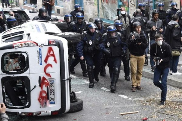 Les CRS et des observateurs à côté d'un véhicule vandalisé par les manifestants.