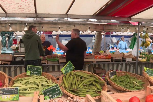 Bastien Gervais (à droite) entouré de ses fruits et légumes, discute avec des collègues et clients au marché de la Porte d'Auteuil