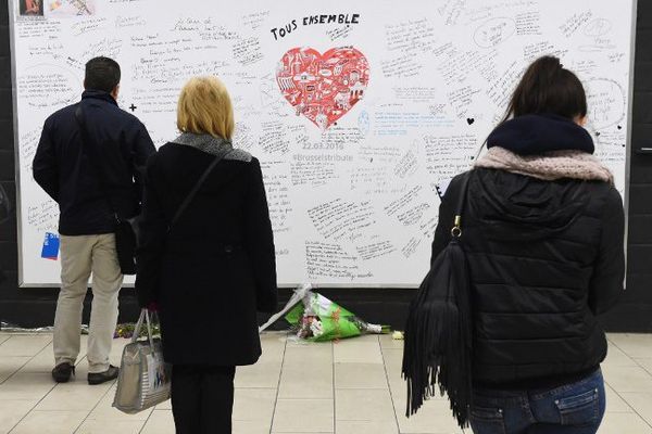 Des usagers lisent les nombreux messages de soutien rédigés sur un grand tableau blanc, accroché dans la station Maelbeek.