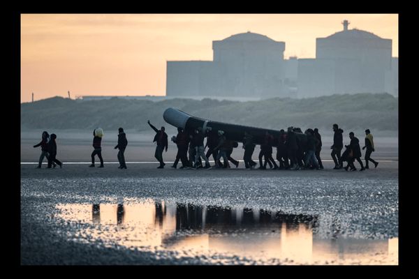 Des personnes s'apprêtent à traverser la Manche à bord d'un bateau pneumatique devant la centrale nucléaire de Gravelines. Il y a un an, le 24 novembre 2021, 31 personnes ont disparu en tentant de rejoindre l'Angleterre, leur eldorado.