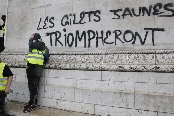 Des manifestants gilets jaunes devant un tag sur l'Arc de triomphe, le 1er décembre 2018.