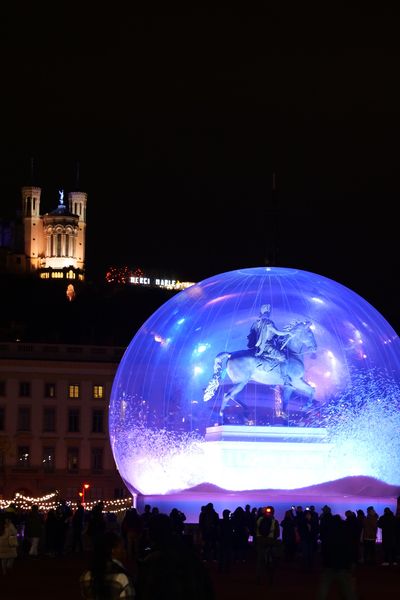 Place Bellecour, la statue se transforme en boule de neige géante, surplombée par la Basilique Notre-Dame de Fourvière.