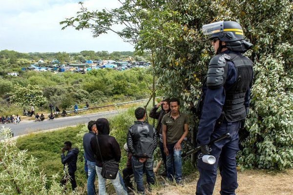 Un CRS debout devant des migrants à Calais en juin 2015. Au loin, la "new jungle" où les migrants vivent dans des conditions sanitaires critiques.
