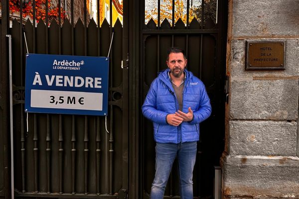 Le président du conseil départemental de l'Ardèche pose devant la préfecture avec le panneau "à vendre".