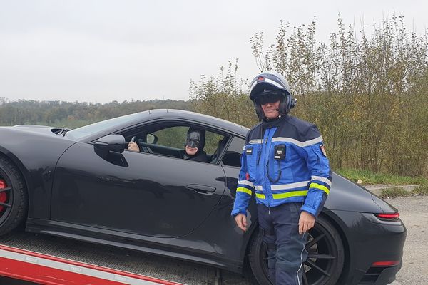 Batman, au volant de sa Porsche immobilisée, prend la pose avec un gendarme ardennais.