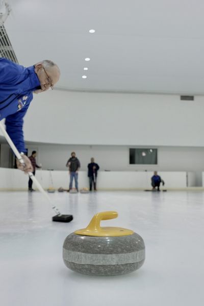 Un joueur de curling balaye la glace, devant la pierre de granit.