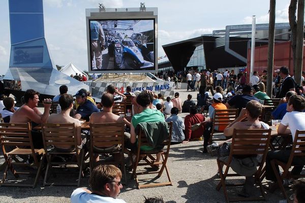 Dans le village des 24 Heures du Mans, des spectateurs regardent l'écran géant qui retransmet la course. 