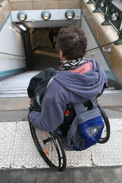 Une personne en fauteuil devant un escalier menant au métro (illustration)