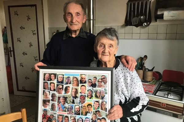 Marinette et Roger posent fièrement devant un montage des photos des enfants et des petits-enfants, préparé à l'occasion de leurs 70 ans de mariage.