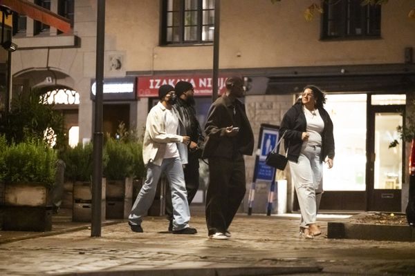 Kylian Mbappé, vêtu d'une veste blanche et portant un masque, déambule avec ses proches  dans le centre de Stockholm.