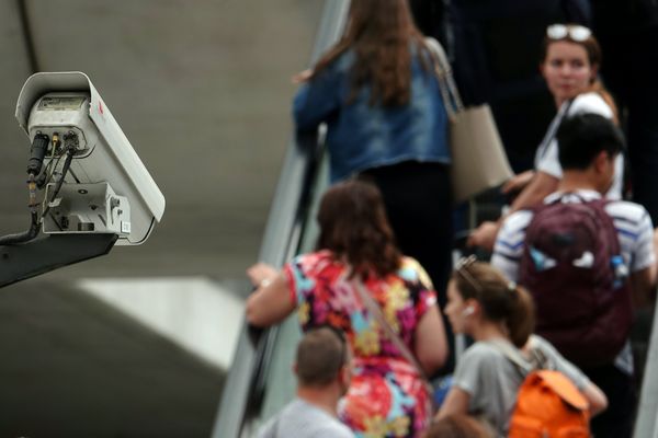 Une caméra de surveillance filment des voyageurs montant sur un escalator dans une gare ferroviaire.