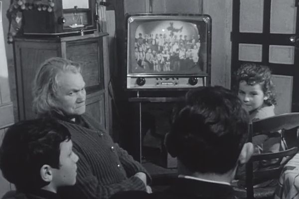 Dans son café de Saint-Georges-de-Gréhaigne (Ille-et-Vilaine), Mme Briand rassemble quelques villageois devant son poste de télévision au début des années 1960.