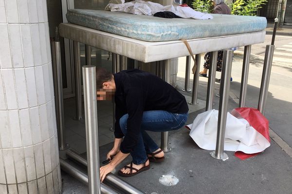 Un homme dévisse les poteaux anti-SDF devant la Caisse d'Epargne à l'angle de la rue d'Alésia et de la rue rue Hippolyte Maindron.