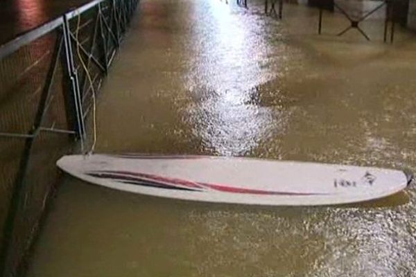 Un cafetier profite de la montée des hauts pour surfer, en attendant de pouvoir estimer les dégâts causés par l'eau.