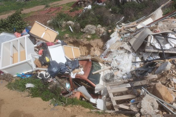 Un amoncellement de gravats, meubles et déchets divers recouvrent l'épave d’une voiture au fond d’une excavation de terre.