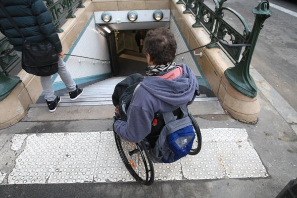 Une personne en fauteuil devant un escalier menant au métro (illustration)