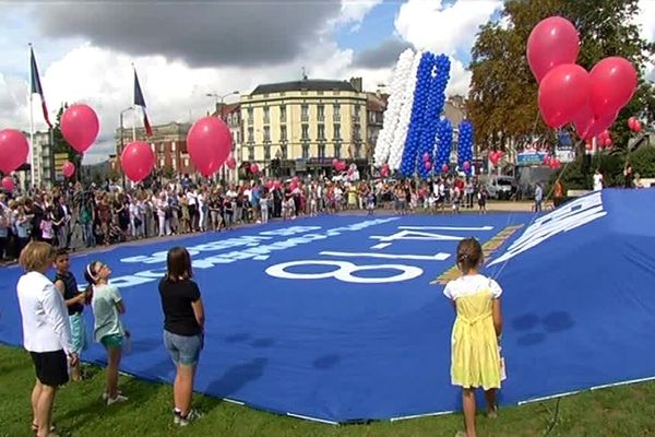 "Reims commémore ses héros" : déploiement du drapeau géant sur les marches du Monument aux Morts.