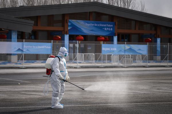 Un membre de l'organisation des Jeux Olympiques de 2022, en combinaison intégrale de sécurité, entrain de désinfecter la zone contre le Covid, aux abords de la compétition.