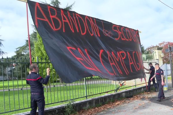 Des sapeurs-pompiers en grève accrochent une banderole aux grilles du Conseil départemental du Lot-et-Garonne.