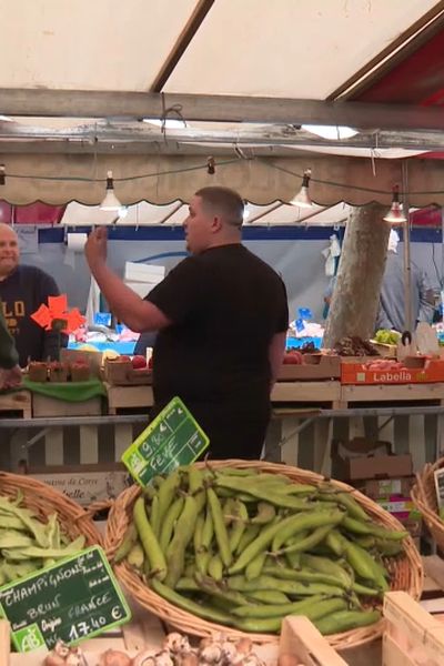 Bastien Gervais (à droite) entouré de ses fruits et légumes, discute avec des collègues et clients au marché de la Porte d'Auteuil