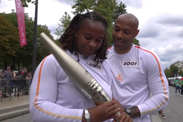 Thierry Henry, ancien capitaine de l'équipe de France de football, passe la main à Romane Dicko pour le relais de la flamme olympique sur les Champs-Élysées, ce dimanche 14 juillet.