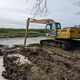 Une pelleteuse effectue des travaux de curage dans la Canche et remonte le limon situé dans le fond du cours d'eau.